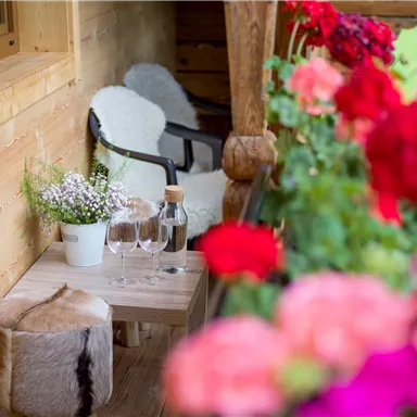 Ein gemütlicher Balkon mit zwei Stühlen, einem kleinen Tisch und einem Strauß Blumen. Bunte Blumen umrahmen die Sicht und schaffen eine einladende Atmosphäre.