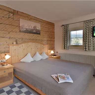 Ein gemütliches Schlafzimmer mit einem Holzbett und angenehm gestalteten Wänden. Der Raum ist hell und modern mit einem TV und stilvollen Gardinen.