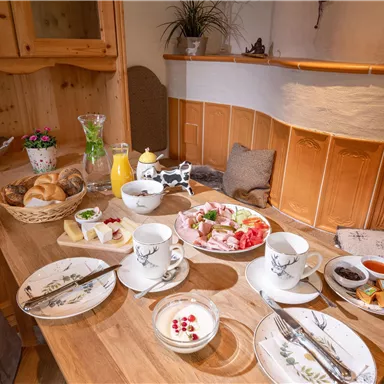 A lovingly set table with various breakfast options, including fresh fruit, yogurt, and pastries. There are also milk, juice, and jam.