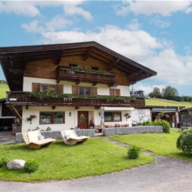 A traditional Alpine house with a large garden. The surroundings are green and spacious, surrounded by gentle hills.