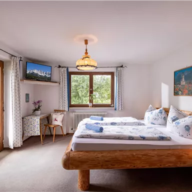 A cozy bedroom with a large bed and wooden details. The room has windows with a view of the outdoors and a modern television.
