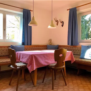 Ein gemütlicher Essbereich mit einer rot-weißen Tischdecke und Holzmöbeln. Die Fenster lassen viel Tageslicht herein und verleihen dem Raum eine freundliche Atmosphäre.