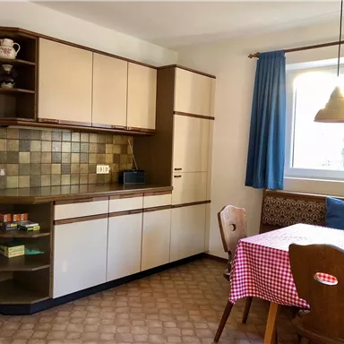 Eine einfache Küche mit hellen Schränken und einer gepunkteten Tischdecke. Es gibt einen Esstisch und eine gemütliche Sitzecke.