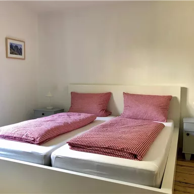 Ein gemütliches Schlafzimmer mit zwei Einzelbetten und roten Kissen. Neben den Betten stehen kleine Nachttische mit Lampen.