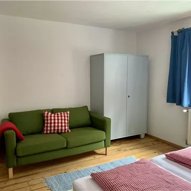 Ein gemütliches Schlafzimmer mit einem grünen Sofa und einem Schlafbereich. Helle Farben und Holzfußboden sorgen für eine einladende Atmosphäre.