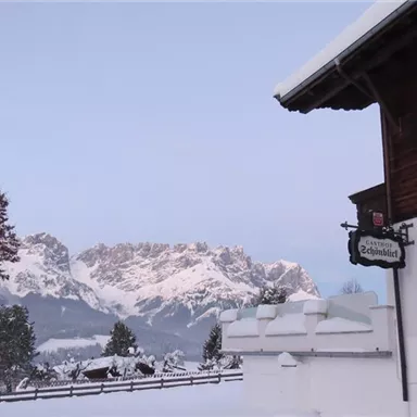 Snow-covered mountains in the background and a charming café in the foreground. The landscape is peaceful and wintry.