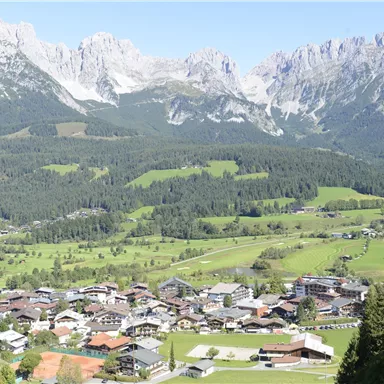 A picturesque mountain landscape with a small village in the foreground. The impressive mountains rise in the background under a clear sky.