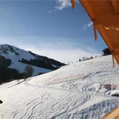 A snow-covered landscape with a mountain in the background. In the foreground, there is a wooden building with beautiful balconies.