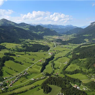Eine malerische Landschaft mit sanften Hügeln, Wäldern und einem klaren Himmel. Im Tal sind kleine Dörfer und Straßen zu sehen.