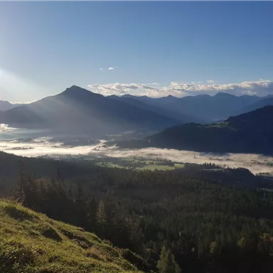 A picturesque mountain landscape with fog in the valley and sun rays shining through the clouds. The scene conveys a sense of tranquility and the beauty of nature.