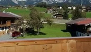 Eine malerische Aussicht auf die Berge mit klar blauem Himmel. Im Vordergrund sind traditionelle Holzhäuser und grüne Wiesen zu sehen.