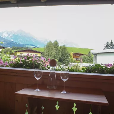 Eine gemütliche Terrasse mit Blick auf die Berge. Auf dem Tisch stehen zwei Gläser und eine Karaffe.