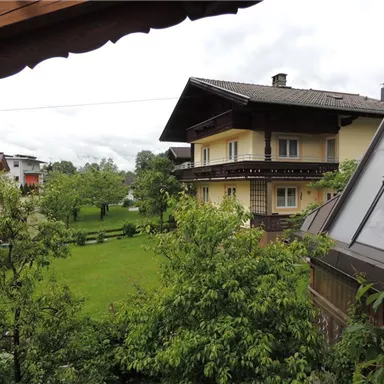 Ein malerisches Wohnhaus umgeben von grünen Bäumen und Wiesen. Im Hintergrund sind die Berge zu sehen, unter einem bewölkten Himmel.