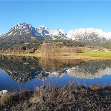 A tranquil landscape with mountains in the background and a clear sky. The lake reflects the surroundings.