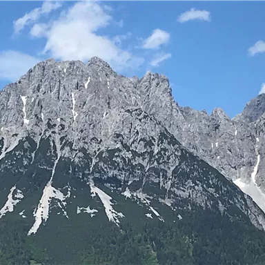Ein majestätischer Berg mit schroffen Felsen und grünen Hängen. Der Himmel ist klar mit einigen wenigen Wolken.