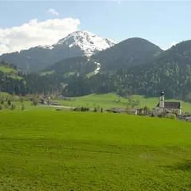 A picturesque landscape with green meadows and snow-capped mountains in the background. In the foreground stands a small church.