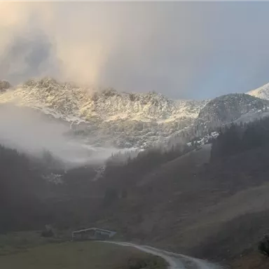 A mystical mountain landscape with snow-capped peaks and fog-covered slopes. In the foreground, a winding path can be seen.