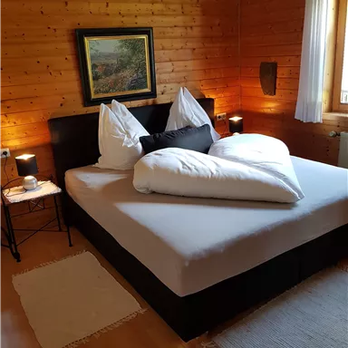 A cozy bedroom with a large bed and many pillows. The walls are made of wood, and the lighting creates an inviting atmosphere.