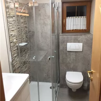 Ein modernes Badezimmer mit Dusche, Waschbecken und Toilette. Steinwandverkleidung und ein Fenster sorgen für Tageslicht.