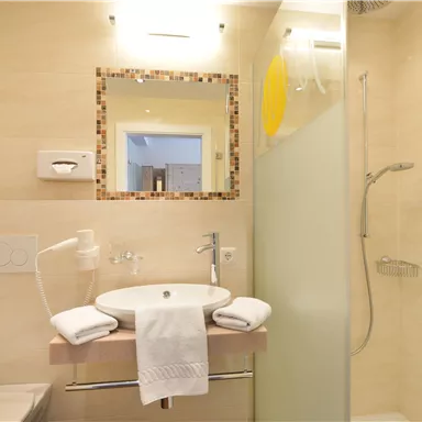 A modern bathroom with a sink and a shower. The walls are designed to be light and simple.