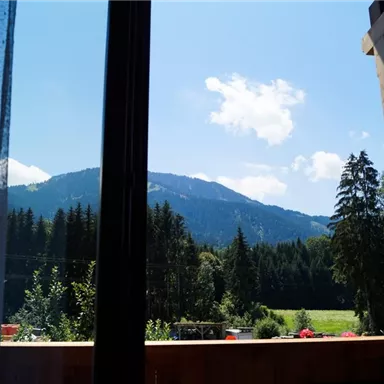 Ein schöner Blick auf Berge und grüne Wälder aus einem Fenster. Der Himmel ist klar mit einigen Wolken.