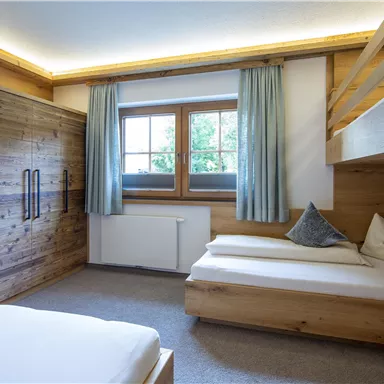 A cozy bedroom with wooden furniture and a window that lets in plenty of light. There is a double bed and a bunk bed, perfect for families or groups.