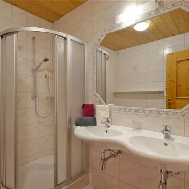 A modern bathroom with a shower and two sinks. The walls are tiled, and there are towels in bright colors.