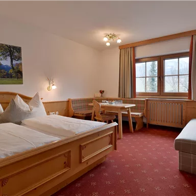 A cozy room with two beds and a dining area. Large windows provide plenty of natural light.