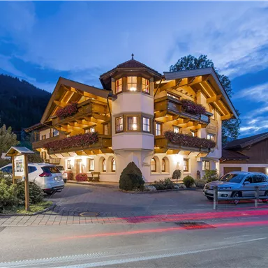 A beautiful building in alpine style with several balconies. The surroundings are surrounded by trees and dimly lit.