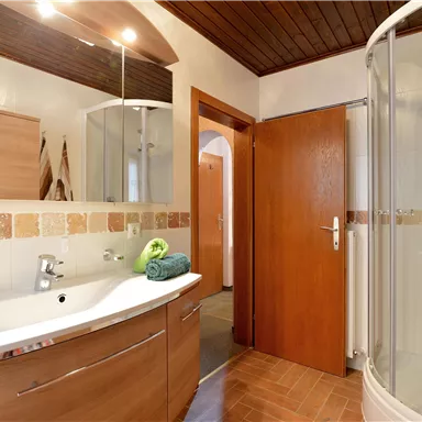 Ein modernes Badezimmer mit einer Dusche und Holzdecke. Die Möbel sind in warmen Holzfarben gehalten und es gibt farbige Handtücher.