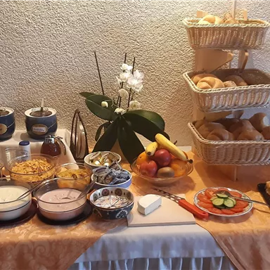 Ein Frühstücksbuffet mit verschiedenen Müslis, Joghurt, frischen Früchten und Brötchen. Dazu gibt es Säfte und Süßgebäck auf einem dekorierten Tisch.