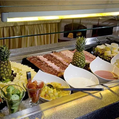 A rich buffet with various types of cheese, platters of cold cuts, and fresh fruit. In the foreground, there are colorful salads and dips.