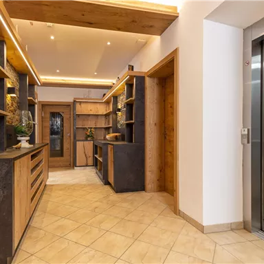 Ein moderner Empfangsbereich mit Holzregalen und eleganten Möbeln. Auf der rechten Seite befindet sich ein Aufzug.