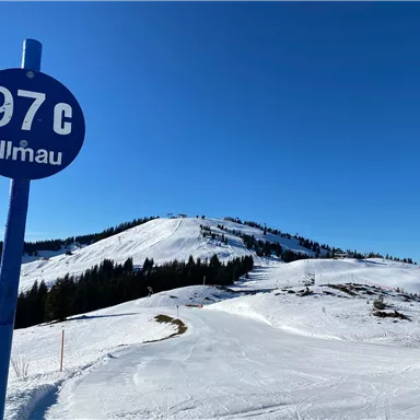Ein schöner Wintertag in Ellmau mit viel Schnee und klarem blauem Himmel. Im Vordergrund steht ein Wegweiserschild mit der Nummer 97.