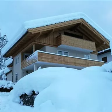 A cozy house with a snow-covered roof. The surroundings are calm and wintry, with plenty of snow.