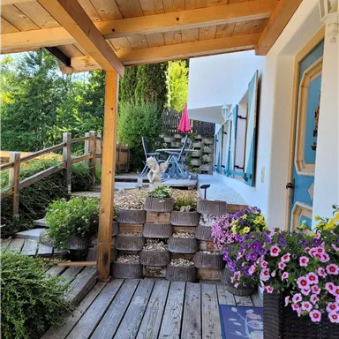 Ein einladender Außenbereich mit Holzdielen und einer gemütlichen Sitzecke. Bunte Blumen und Pflanzen verleihen dem Raum einen frischen, lebendigen Eindruck.