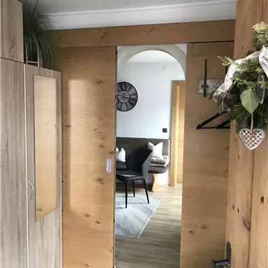 An inviting hallway with a wooden sliding door. In the background, there is a cozy seating area with a gray rug and a clock on the wall.