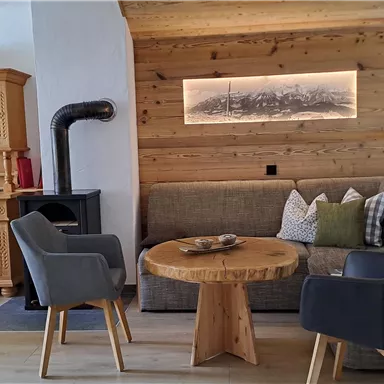 A cozy living room setting with a wooden table, two chairs, and a couch. The space has a warm wooden paneling and a cozy atmosphere.