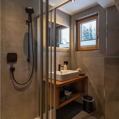 Ein modernes Badezimmer mit einer Glasdusche und Holzregal. Durch das Fenster scheint Tageslicht herein.