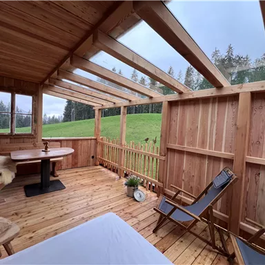 Eine gemütliche Veranda aus Holz mit Blick auf eine grüne Wiese. Die Umgebung ist ruhig und einladend, ideal zum Entspannen.