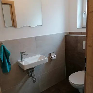 A modern bathroom with a small sink and a toilet. The walls are kept light and a turquoise towel complements the decor.