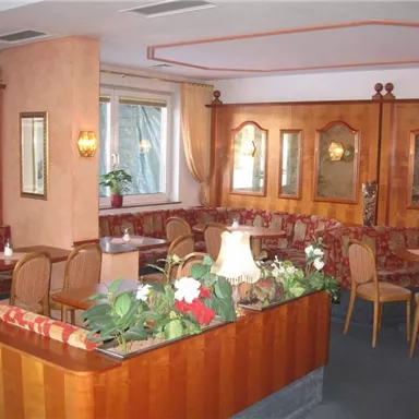 Eine gemütliche Café-Atmosphäre mit Holzinterieur und gepolsterten Bänken. Am Tisch stehen Pflanzen und Kerzen für eine einladende Stimmung.