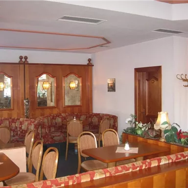 Ein gemütliches Restaurant mit Holzmöbeln und warmen Farben. Die Einrichtung umfasst Tische, Stühle und dekorative Spiegel.