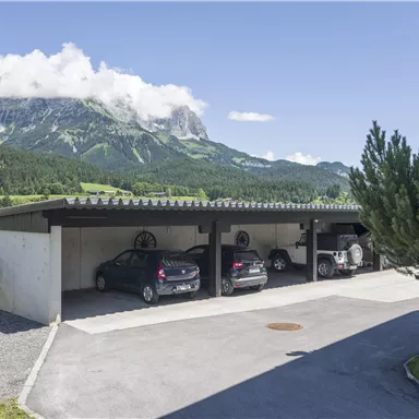 A modern parking garage with several cars in a beautiful mountainous landscape. In the background, there are high mountains and a clear blue sky.