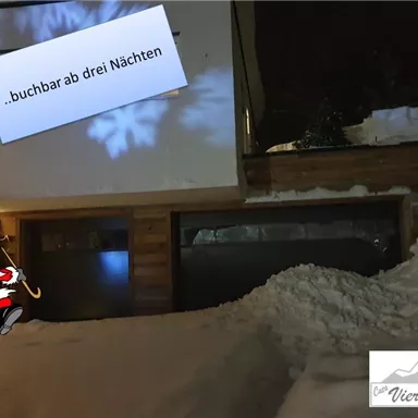 Ein winterliches Szenario mit einem Gebäude im Schnee. Es ist dunkel, und ein Hinweis zeigt, dass Buchungen ab drei Nächten möglich sind.