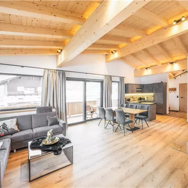 Ein modernes, helles Wohn- und Esszimmer mit Holzbalkendecke. Der Raum ist elegant eingerichtet und bietet große Fenster mit Ausblick.