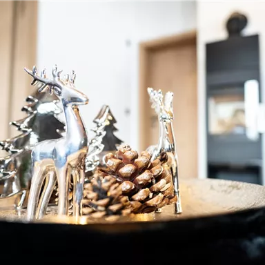 Ein dekorativer Tisch mit silbernen Rehen und einer Tannenzapfen. Im Hintergrund sind Holz- und schwarze Designelemente sichtbar.