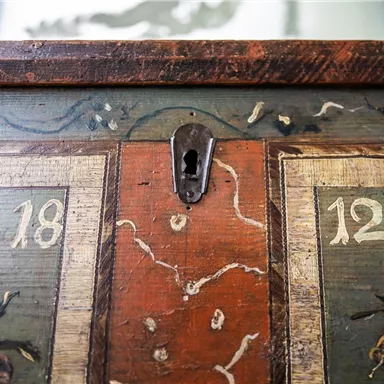 Eine alte, künstlerisch gestaltete Truhe mit bunten Verzierungen und Zahlen. Der Schlüsselverschluss ist gut sichtbar in der Mitte.