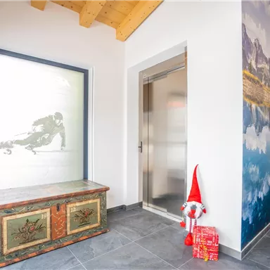 Ein heller Eingangsbereich mit einem traditionellen Holzschrank. An der Wand ist ein großes Bild einer Berglandschaft zu sehen.