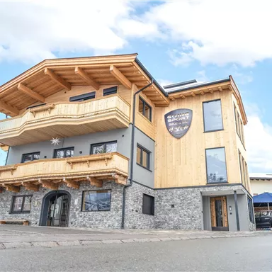 Ein modernes Gebäude mit traditionellem Holzdesign und steinfarbenen Akzenten. Der Himmel ist klar und es sind einige Wolken sichtbar.